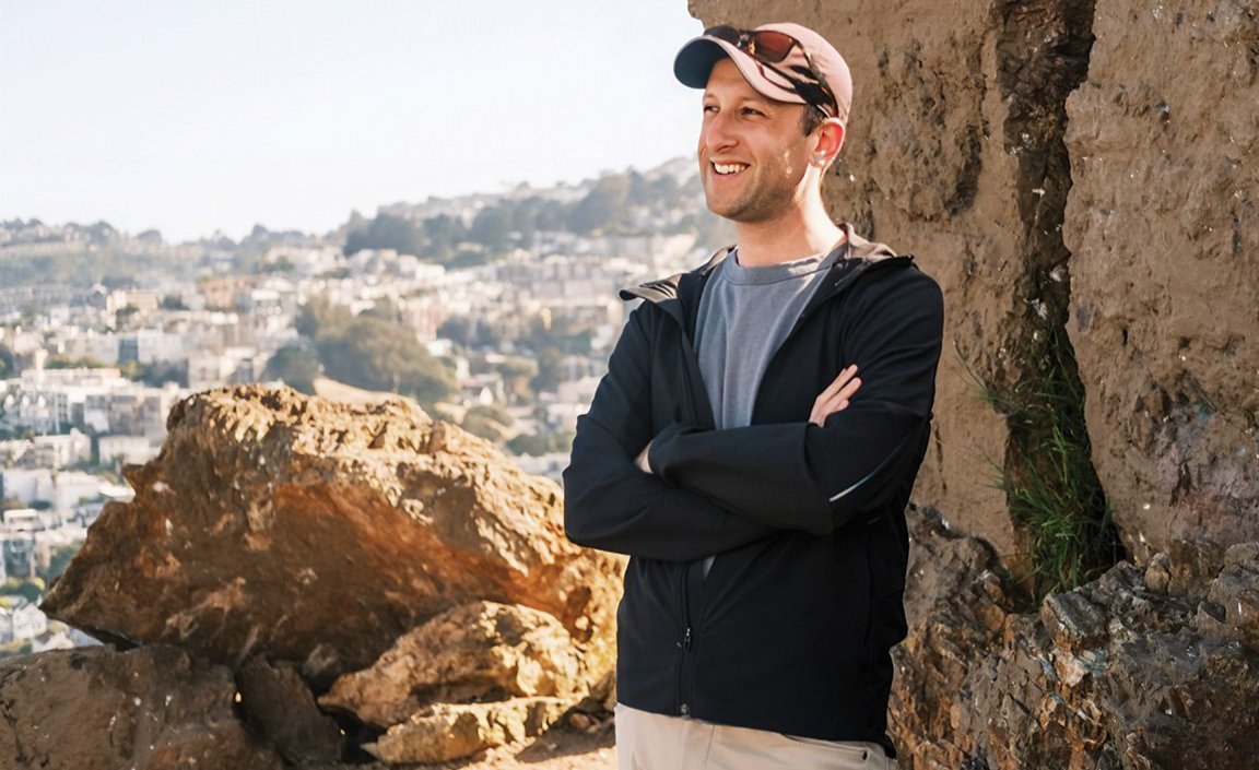 Noah Henry-Darwish stands in front of a rocky cliff wall