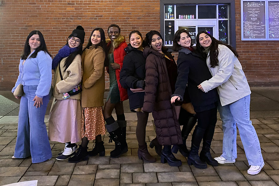 A group of students pose for a photo in front of a brick storefront.