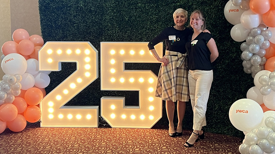 Two people pose by a large, lit-up “25” prop.