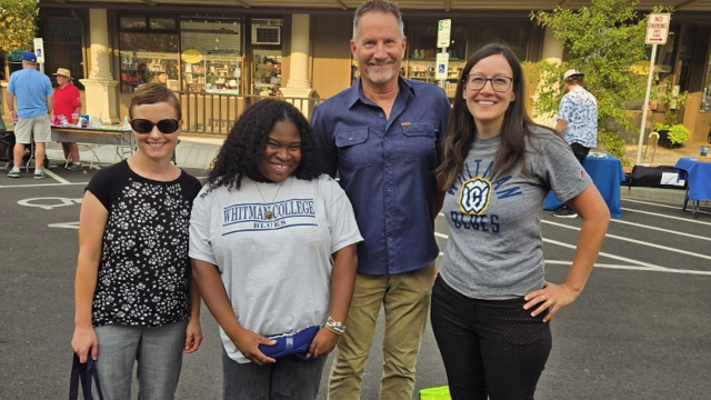 A group of four people pose for a photo in a parking lot with a storefront visible in the background.
