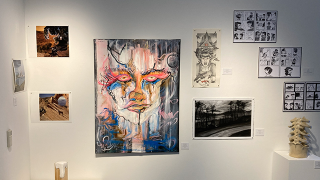 A large abstract portrait along with several other art pieces are displayed on a gallery wall