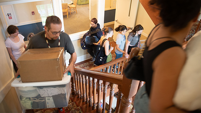 People moving up and down a crowded staircase, some carrying boxes.