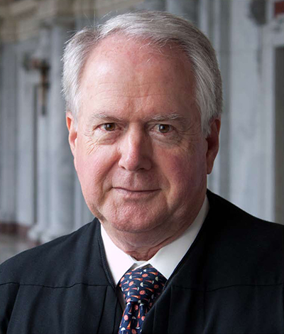 Portrait of William A. Fletcher with short gray hair, wearing a black robe over a suit and tie.