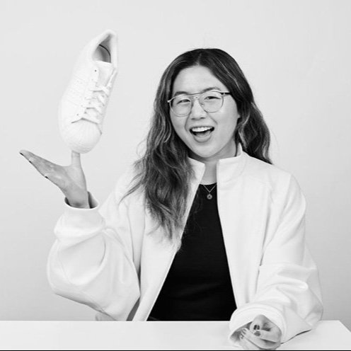 alt=Black and white image of Ashley Joe smiling and lightly tossing an Adidas Superstar up in the air.