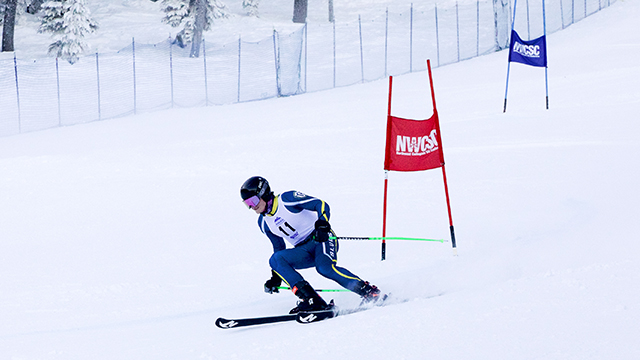 Elias Kean ’27 skiing down a snow-covered run with one red flag and one blue flag seen behind them