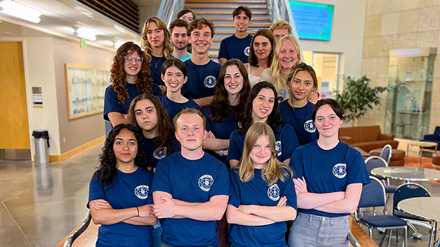 A group of students wearing matching shirts stand at the bottom of a staircase.