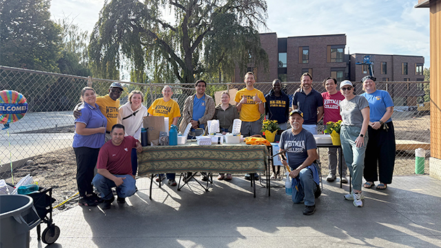 A group of volunteers, most wearing Whitman College shirts, gathered at a table positioned near an entrance to Harvey Hall.