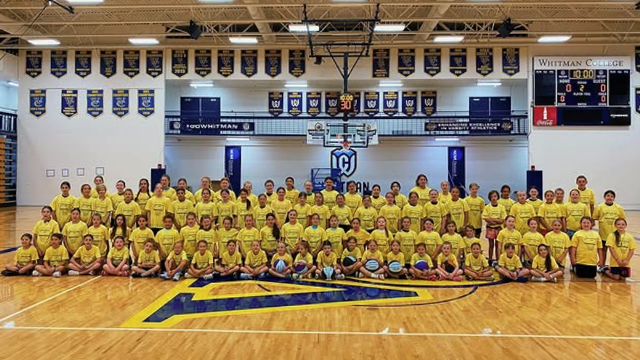 A large group of young athletes wearing yellow shirts, pose for a photo on a basketball court.