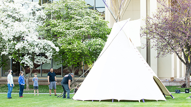 Five people stand next to a tipi on the south lawn by Cordiner Hall.