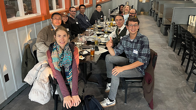 A group of people pose for a photo while seated around a long table in a restaurant setting.