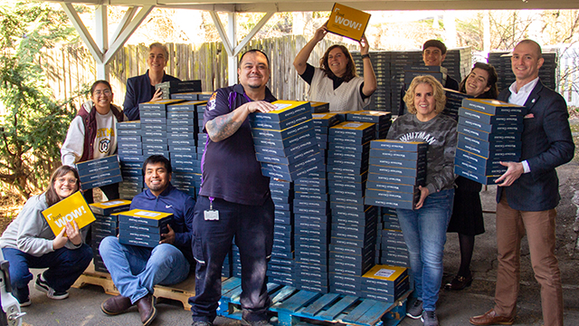 A group of Whitman employees stand with large stacks of blue and yellow boxes.