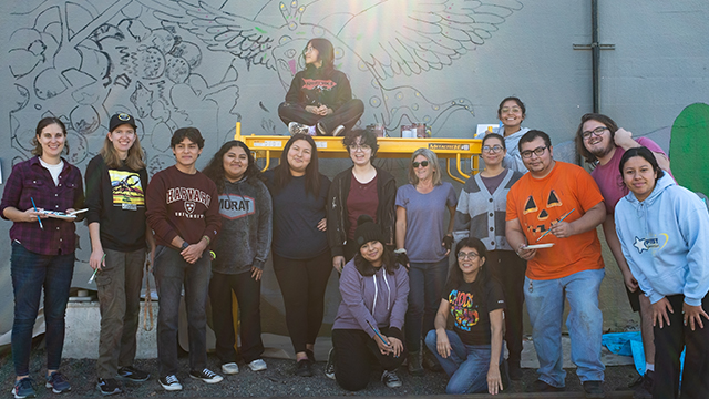 A group of people standing in front of wall with the outlines of a mural