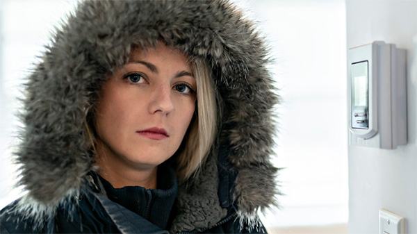 Upset woman in parka next to thermostat.