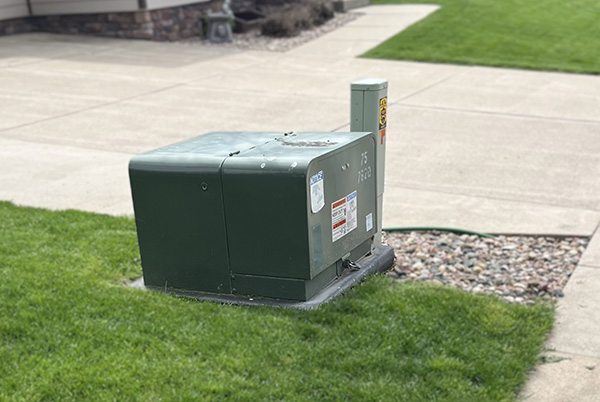 Green pad-mounted transformer on grassy lawn near concrete driveway.