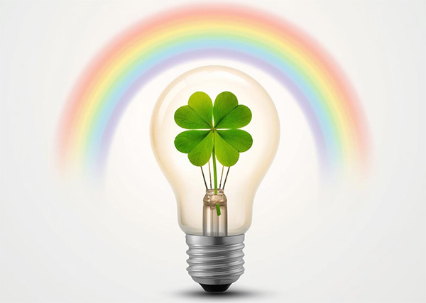 Four leaf clover in a light bulb underneath a rainbow.
