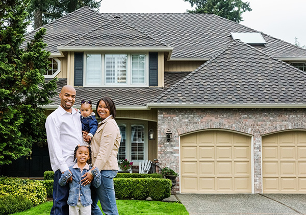 Smiling family of four standing in front of two-story brick home.