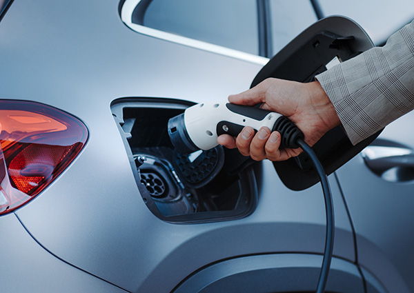Man holding electric vehicle charger by car.