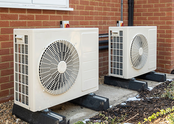 Two heat pumps next to a brick wall.