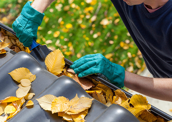 Man with gloves and a shovel cleaning leaves out of a gutter.
