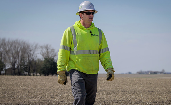 Photo of Tanner wearing hard hat, walking through harvested field.