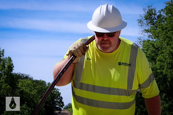 MPC lineman wearing hardhat, carrying cord outside.