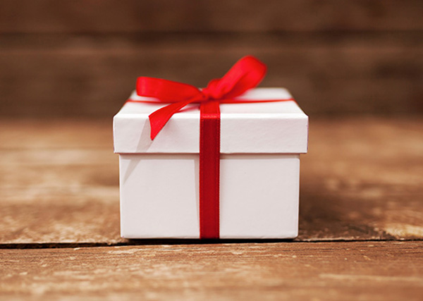 White gift box with red ribbon on wood table.