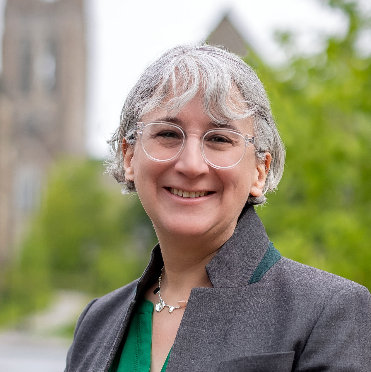 Rebecca Lowenhaupt in green top and grey jacket in front of campus background