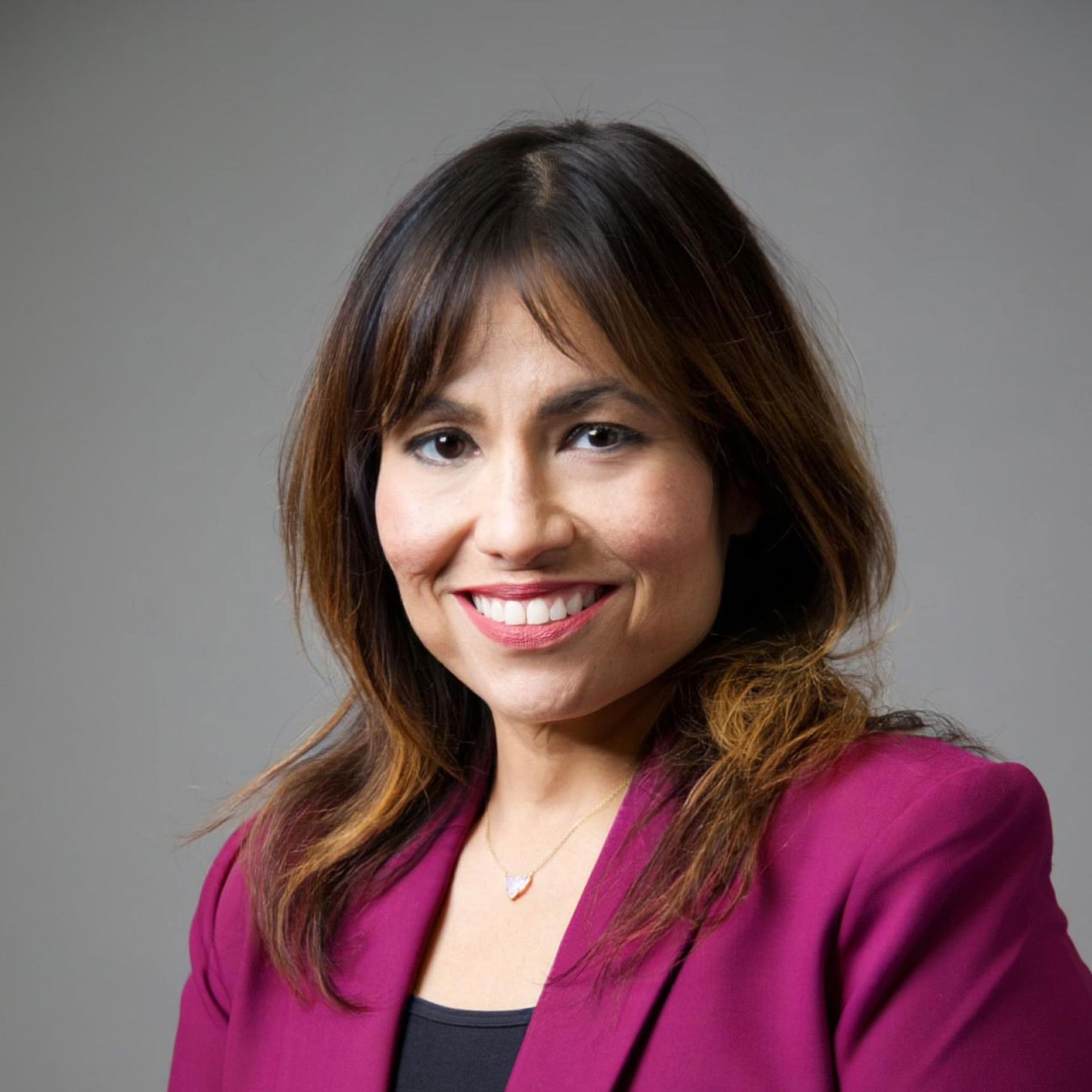 Stella Flores in maroon jacket against grey background
