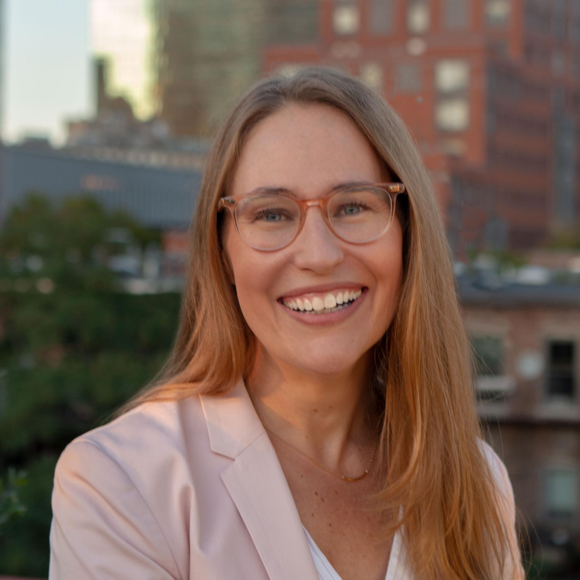 Angela Boatman in light colored jacket against cityscape background