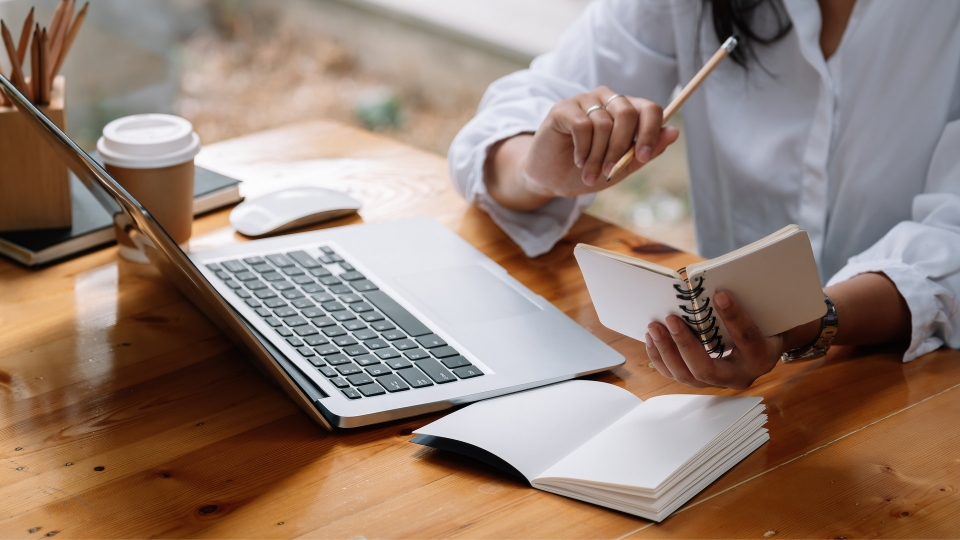 Person working on a computer with a notebook and coffee