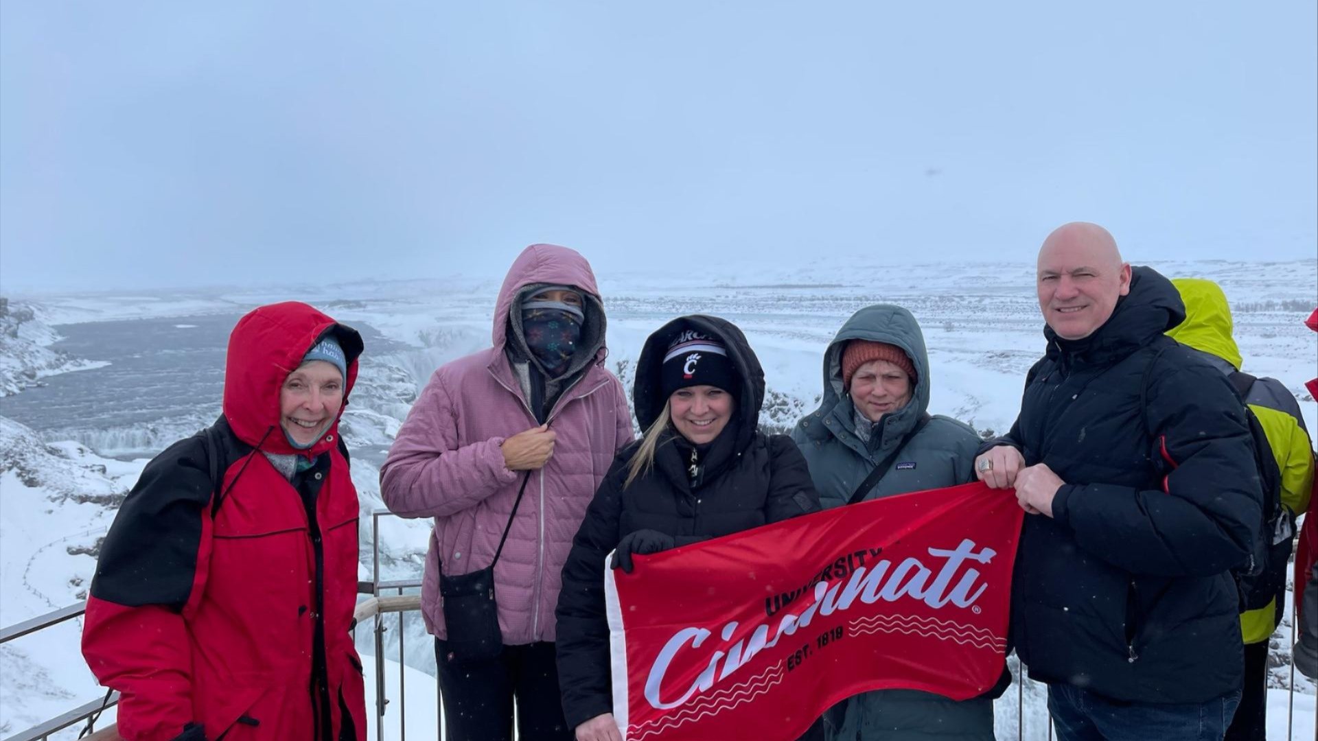 UC alumni posing with UC flag in a wintery setting