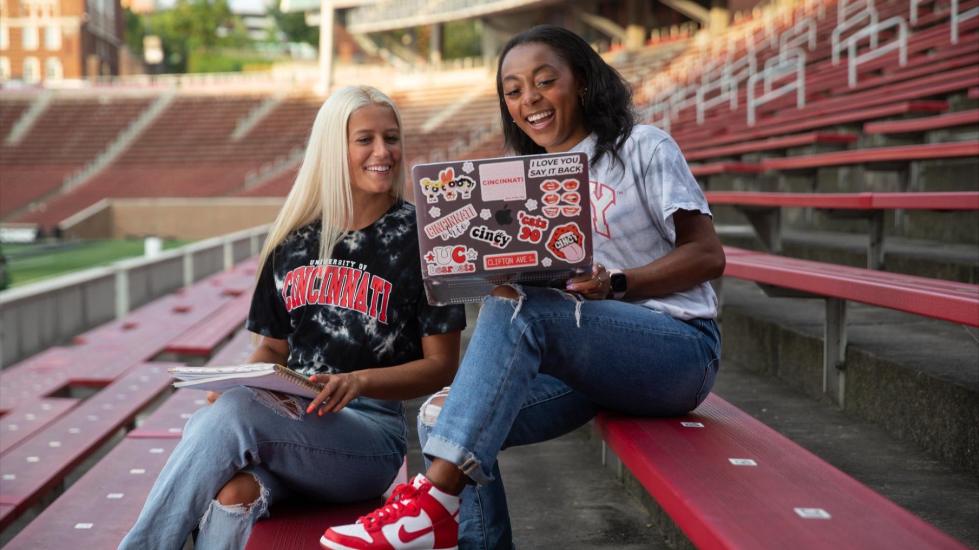 Two students looking at a laptop while smiling in Nippert Stadium. 
