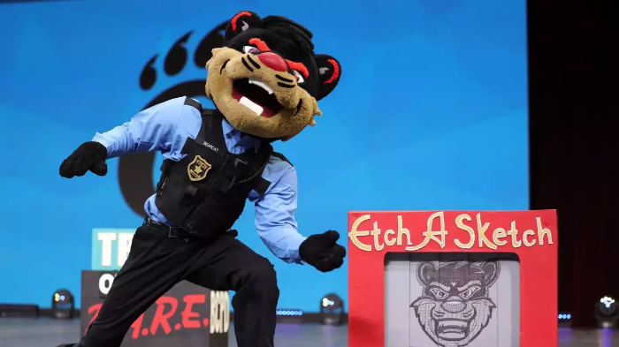 University of Cincinnati mascot posing in a police uniform next to a large Etch A Sketch drawing of their face.