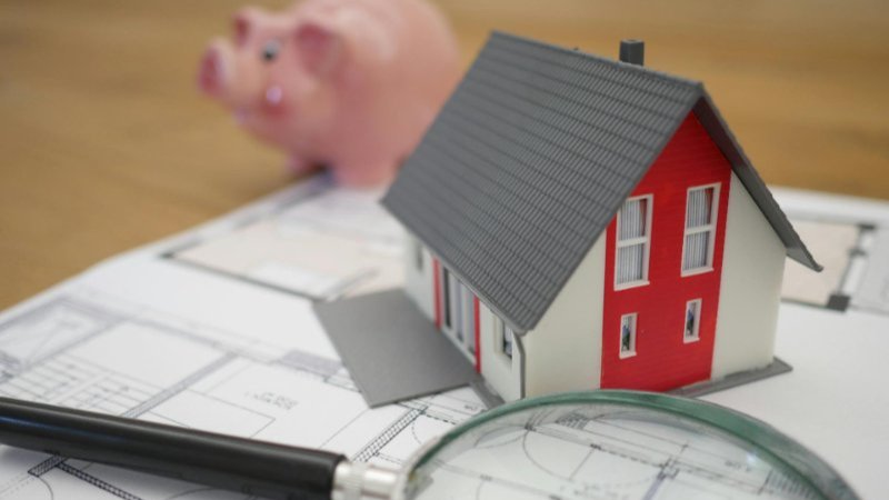 A piggy bank, model of a house and a magnifying glass