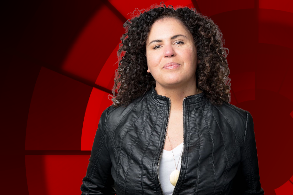 Image of Safiya Umoja Noble smiling in front of a red background.
