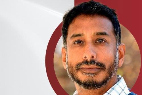 Image of Anand Pandian smiling in front of a red and white background.