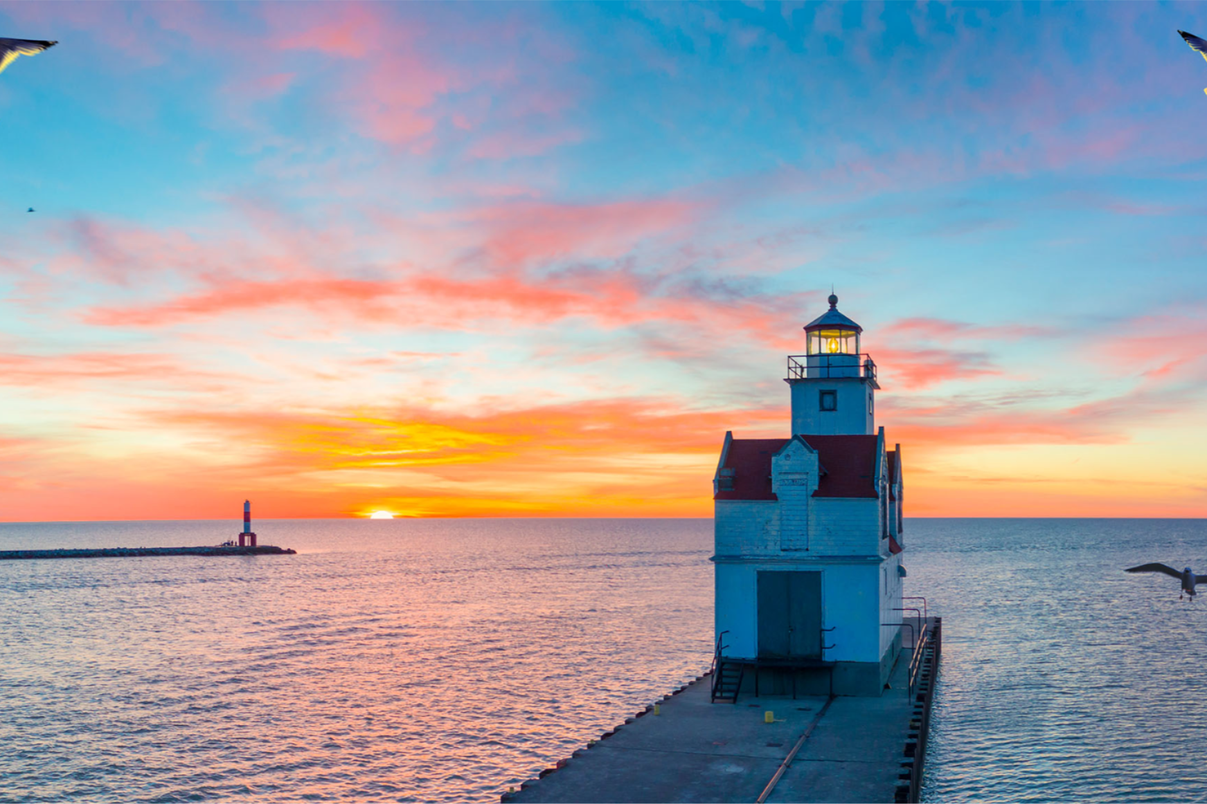 A lighthouse at the Great Lakes in the background is a sunset.