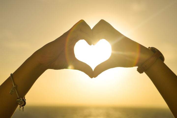 Image of sunset with hand heart at the forefront of the image
