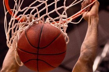 Image of basketball hoop with basketball going through and man hanging on the rim