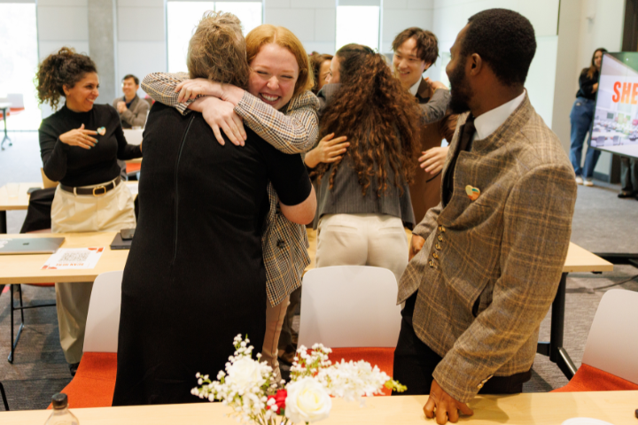 A group of people hugging at the Shark Tank competition.