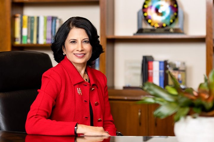 Image of President Khator wearing a red coat and smiling in her office.