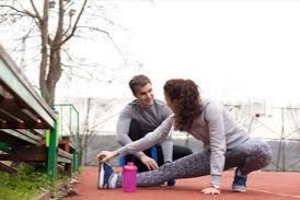 Image of woman stretching on a track in workout attire; man kneeling next to hear 