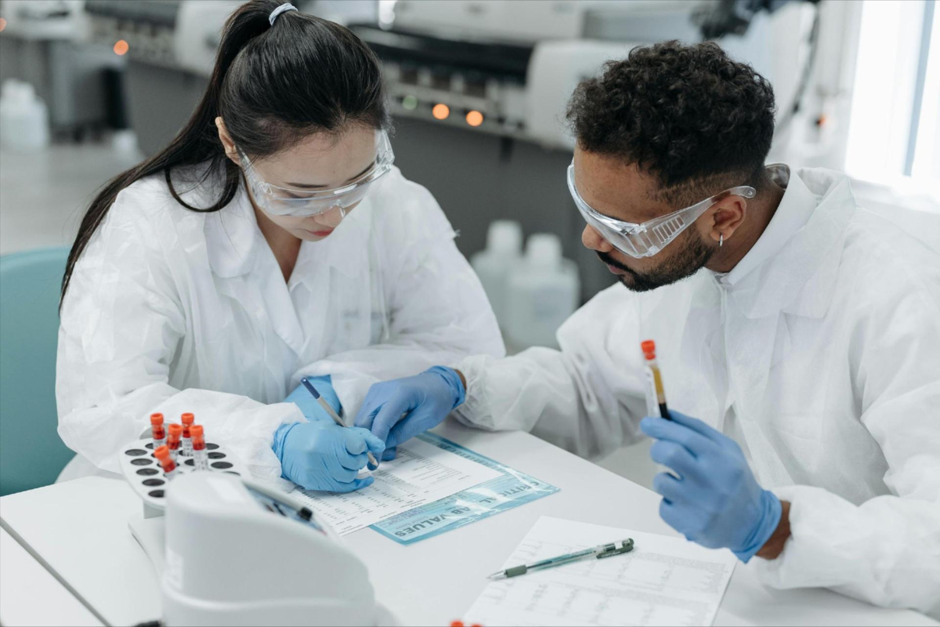 A man and woman in white coats and goggles looking at a test tube.