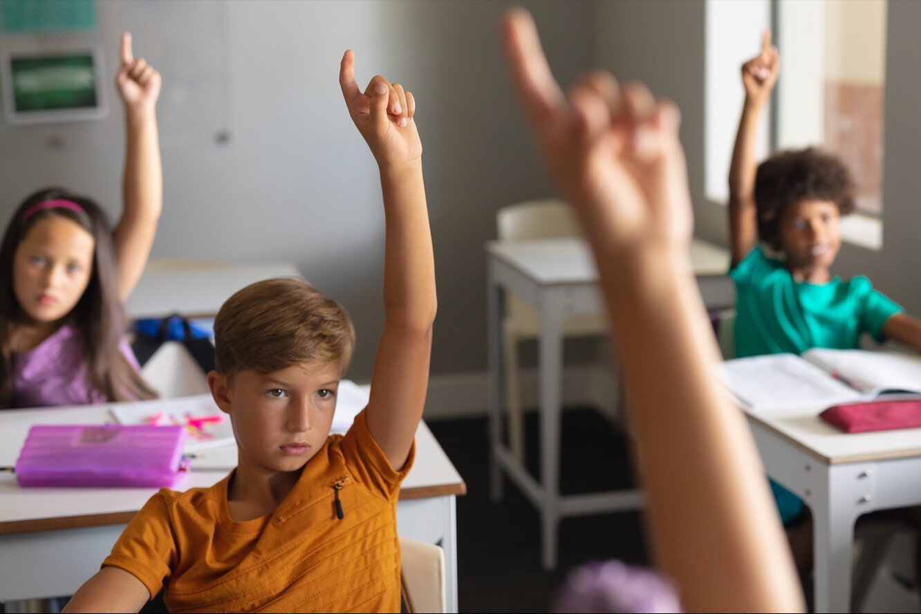 a group of kids raising their hands in a classroom