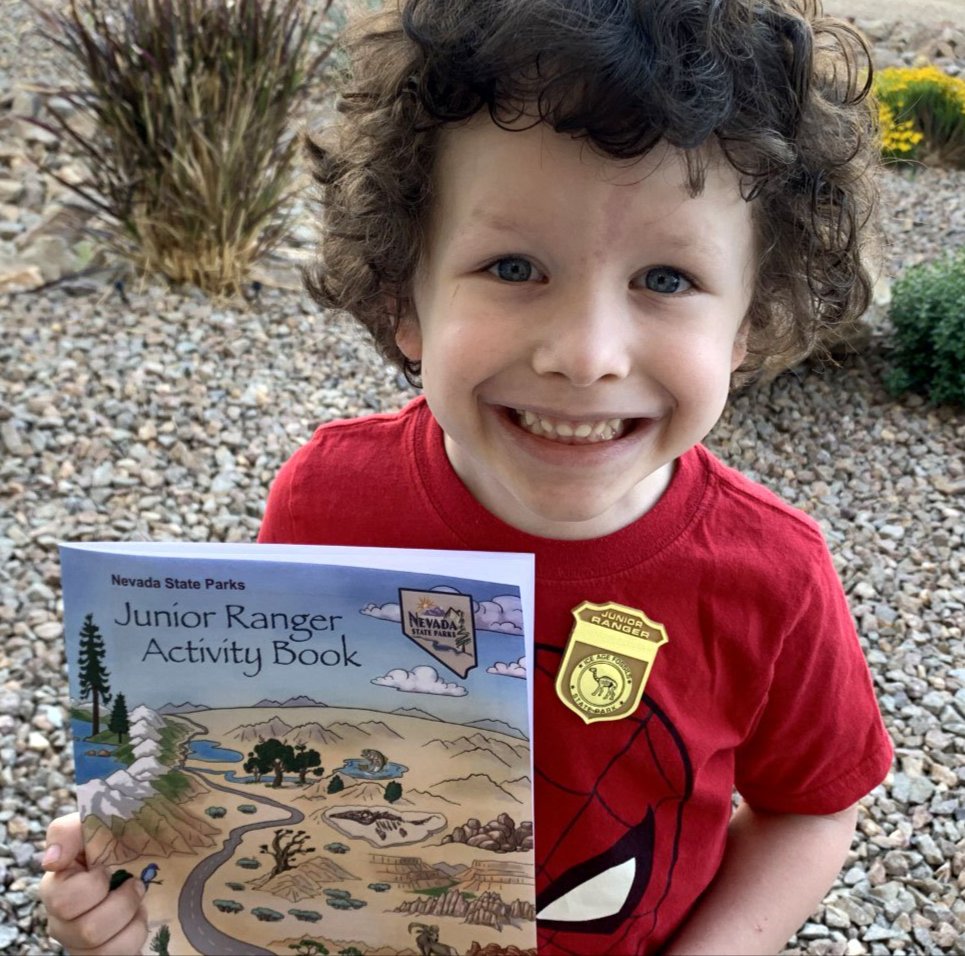 A child holding the Junior Ranger Activity Book wearing a red shirt and smiling at the camera