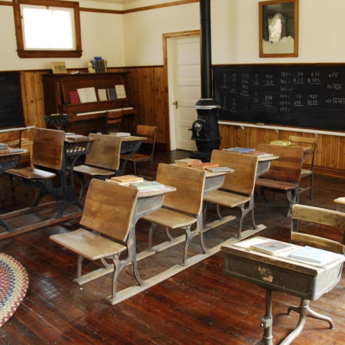 A one-room school house with desks, a chalkboard, and a piano