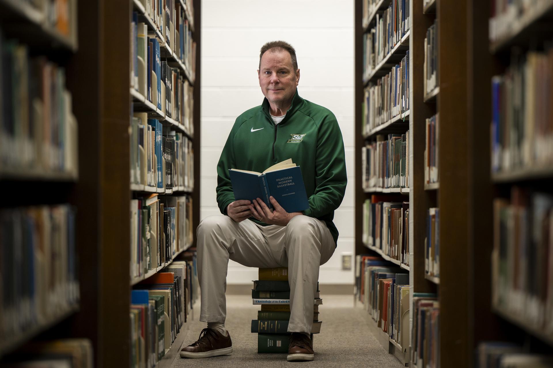 A man sitting on a stack of books in the Curtis Laws Wilson Library.