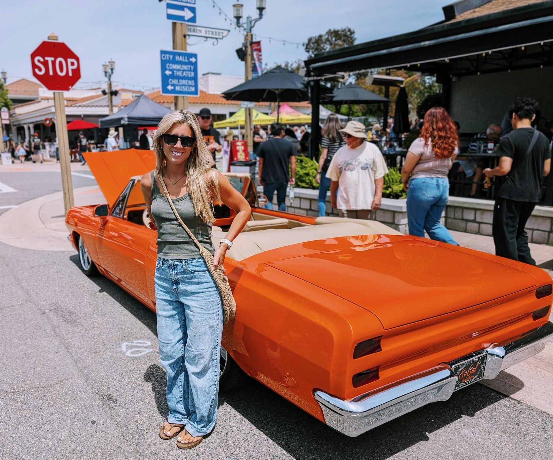 Ashley at the Temecula Rod Run with an orange classic car in Old Town Temecula