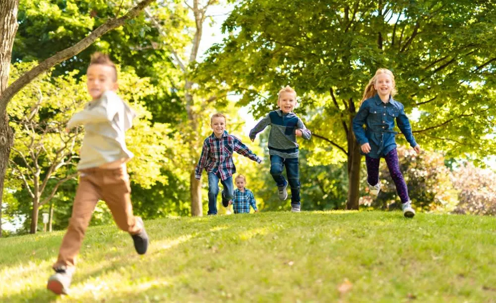 Five Children Running in grass with tall trees in the background