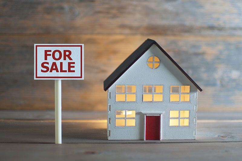 A sign on photo reads "For Sale." A beautiful minature home that is lighted inside with a red door.